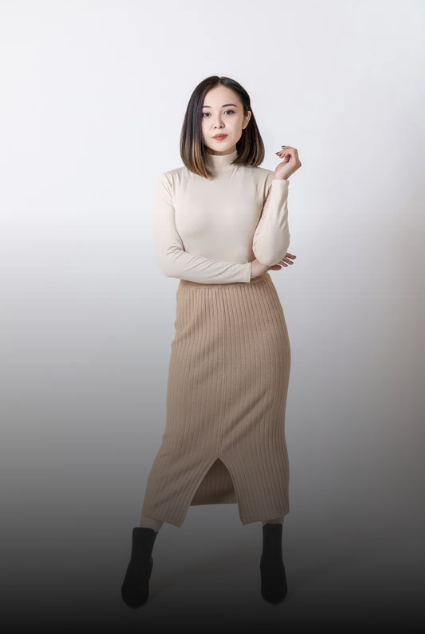 Full-body shot of a woman in a cream turtleneck and beige knit midi skirt, standing with one arm crossed and the other hand near her face against a white backdrop.